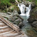 A bridge on the Owyhigh Trail crosses Chinook Creek near Deer Creek Camp. The waterfall cascades into a clear green pool.