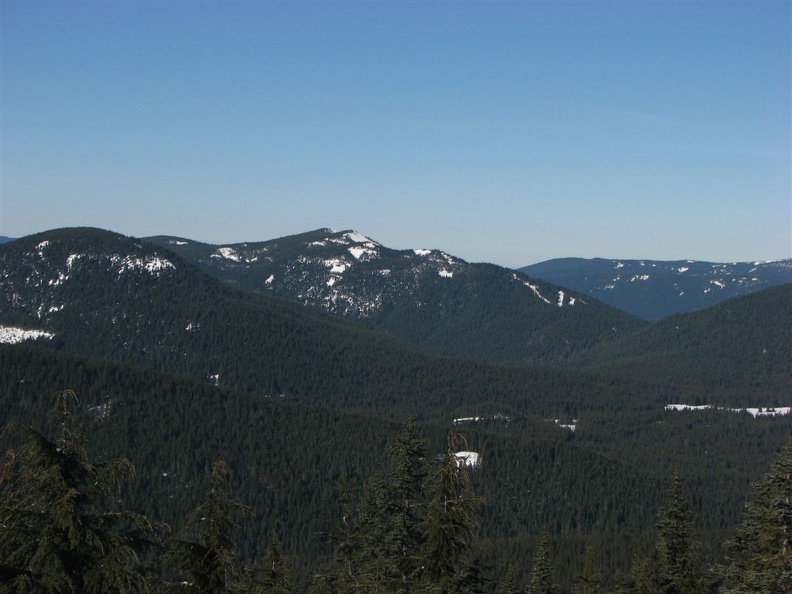 A forested and snow covered ridge of hills looking east from above Frosty rocks on the shady side of the ridge. This is on a promontory west of the Pacific Crest Trail between Barlow Pass and Twin Lakes.