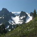 Mt. Rainier is the white mass in back of Sluiskin Mountain. A sloping field of avalanche lillies decorate the nearby hillside.