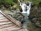 A bridge on the Owyhigh Trail crosses Chinook Creek near Deer Creek Camp. The waterfall cascades into a clear green pool.